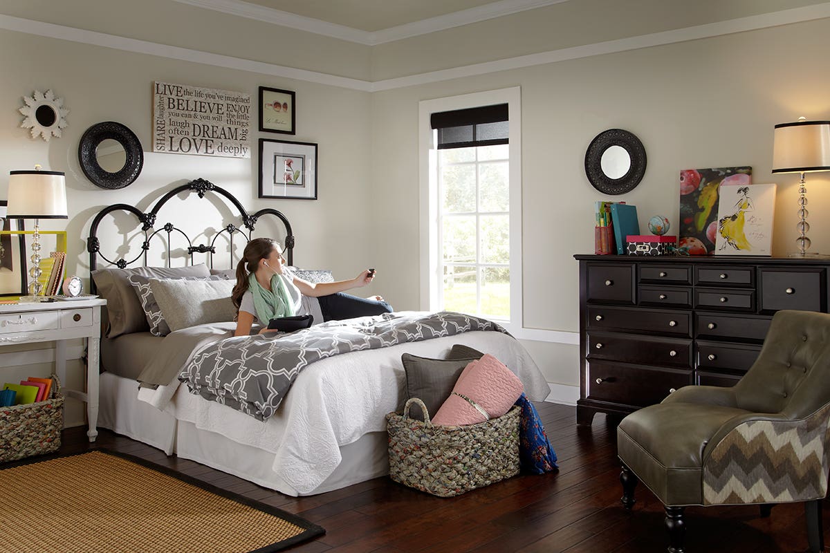 Woman Laying in Bed Closing Sheer Roller Shades with Remote Control