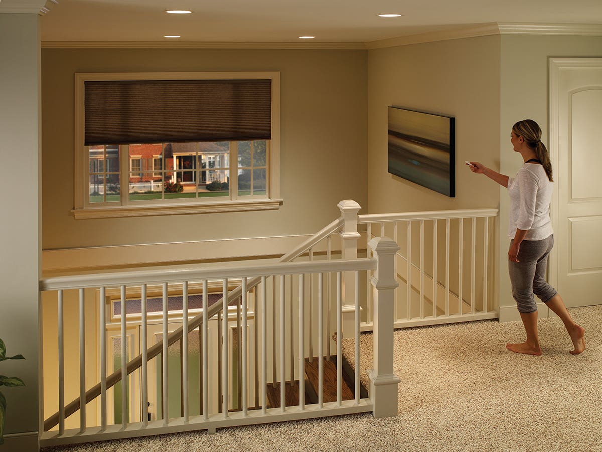 Woman on second story of foyer with remote control closing single-cell inside mount honeycomb shades