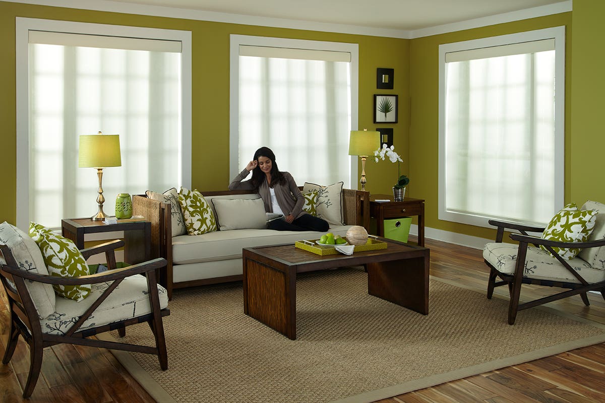 Woman sitting in bright green sunroom with closed white roller shades