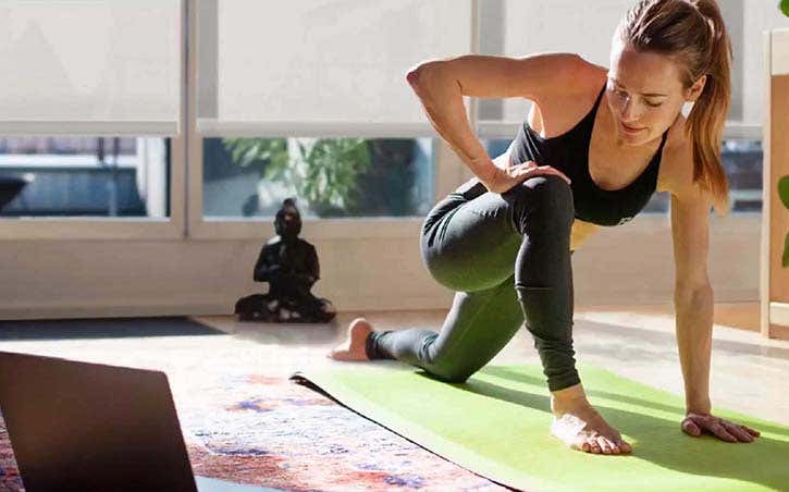 Woman doing yoga on a green mat with smart shades partially closed behind her