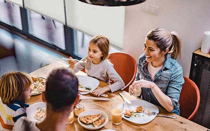 Family of four at a table eating a meal with motorized smart blinds in the windows